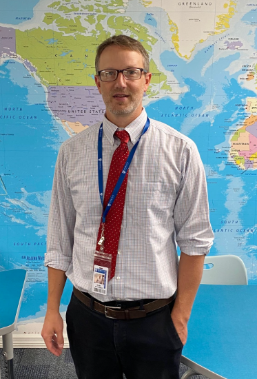 SMILES ‘ROUND THE WORLD: Mr. Wahlgren smiles for a photo in his Honors/AP US  history classroom.